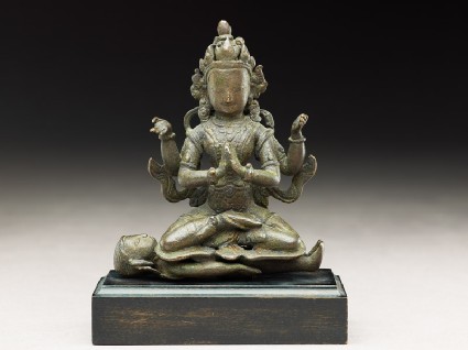 Seated figure of a crowned deity with four arms upon another figureside