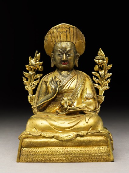 Seated figure of a monk with two flowers, a sword, and scripturesfront